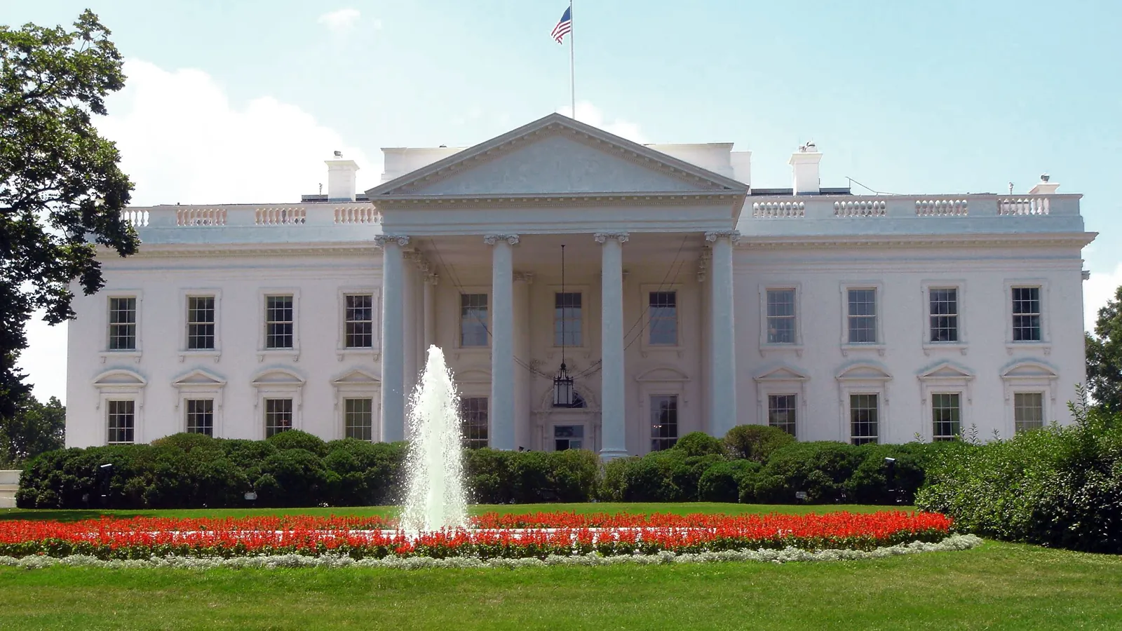 The north front of the White House with its fountain, lawn and red flower beds under a clear sky