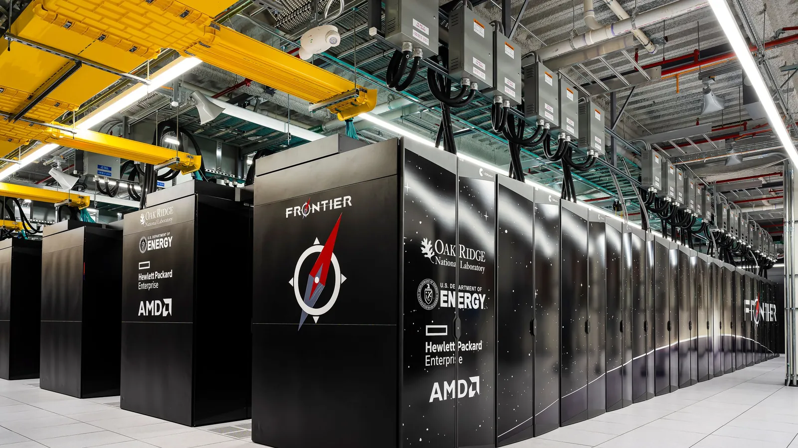 Rows of black Frontier supercomputer cabinets under yellow cable trays at Oak Ridge National Laboratory