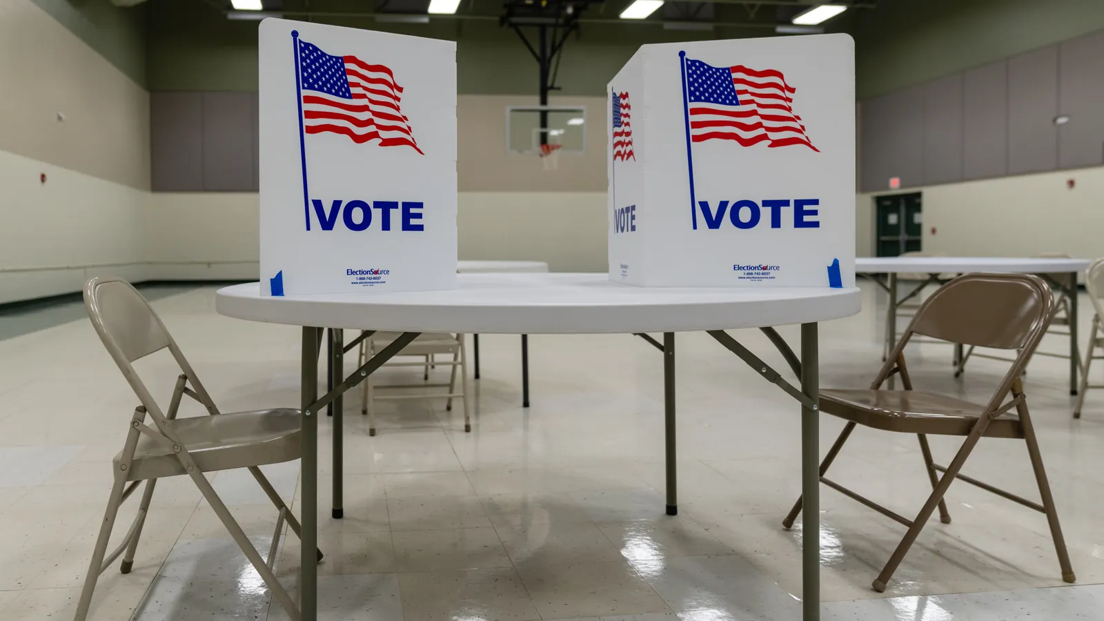 Two white voting booths printed with the US flag and the word Vote on a table in a polling place