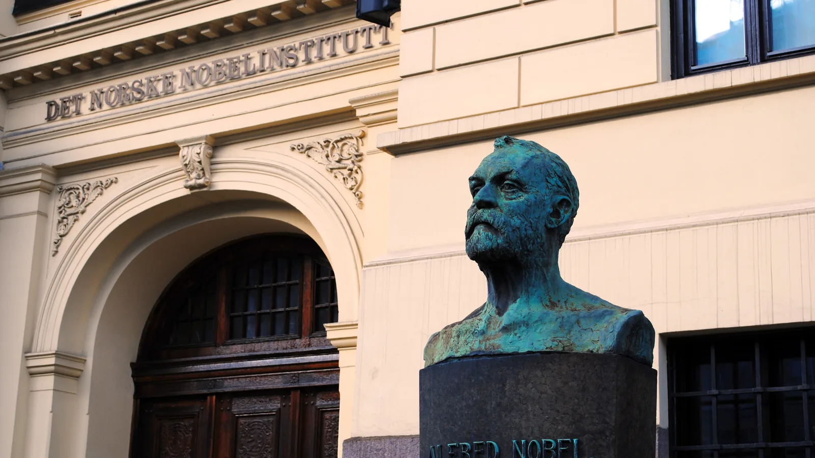 Bronze bust of Alfred Nobel in front of the arched entrance of the Norwegian Nobel Institute in Oslo