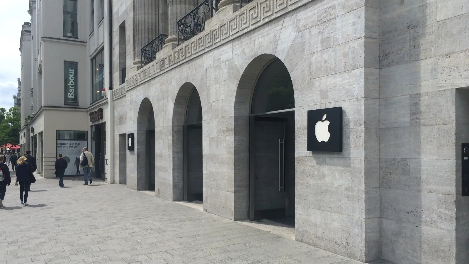 The stone arcade of the Apple Store on Kurfürstendamm in Berlin, with the Apple logo beside its arched entrance and people walking past