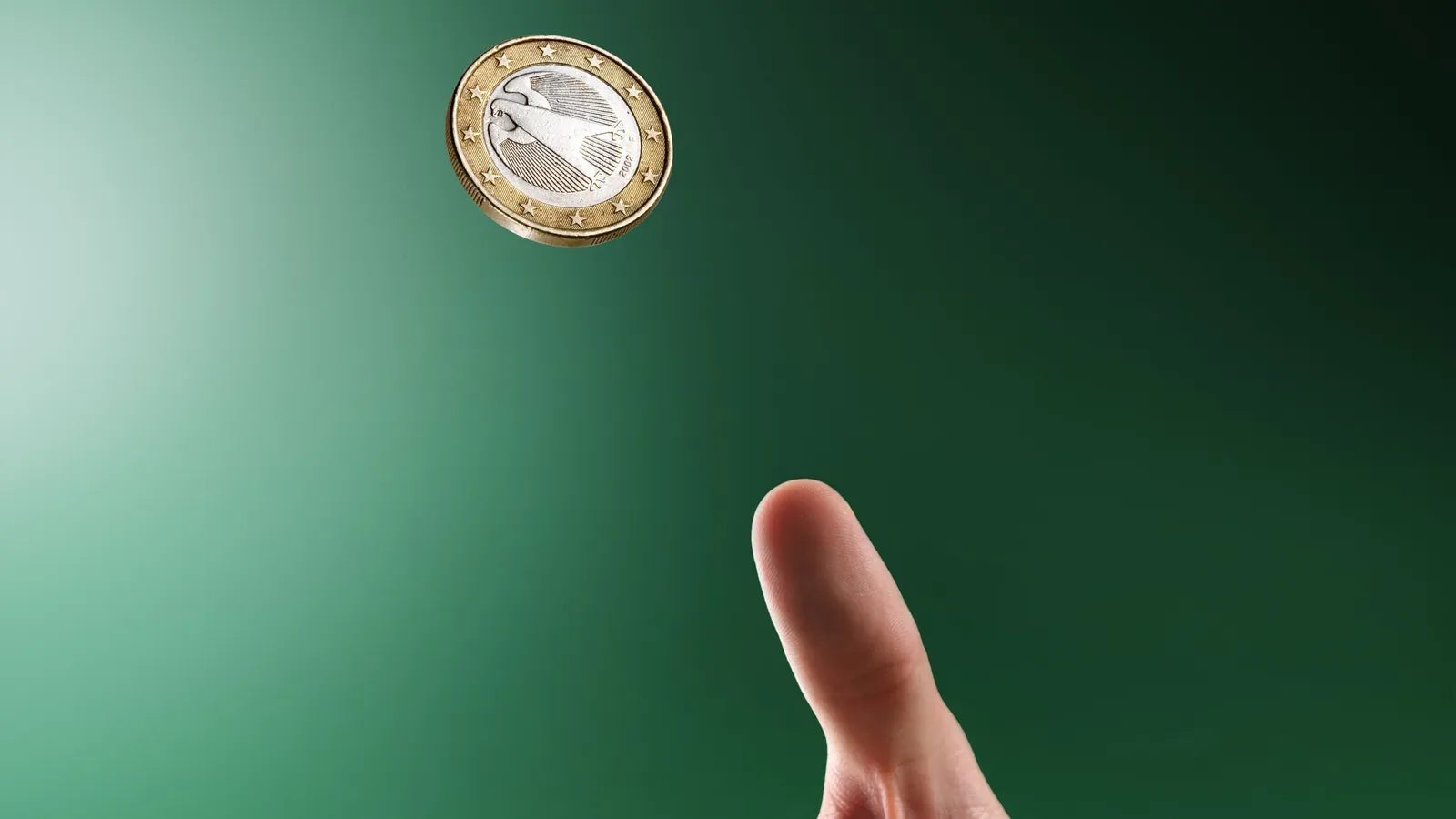 A one-euro coin spinning in the air above the thumb that flipped it, against a green backdrop