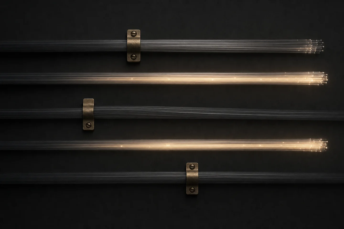 Five fibre-optic bundles cross a dark surface; three are held by brass clamps and stay dark, two glow gold