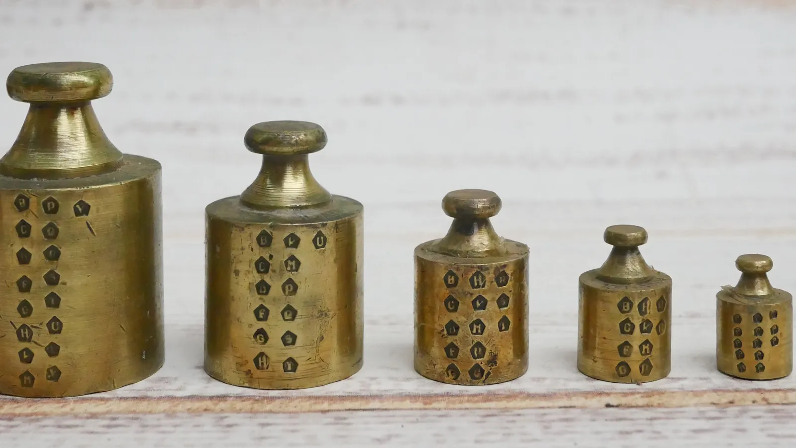 Five French brass weights in a row from largest to smallest, each covered in stamped verification marks