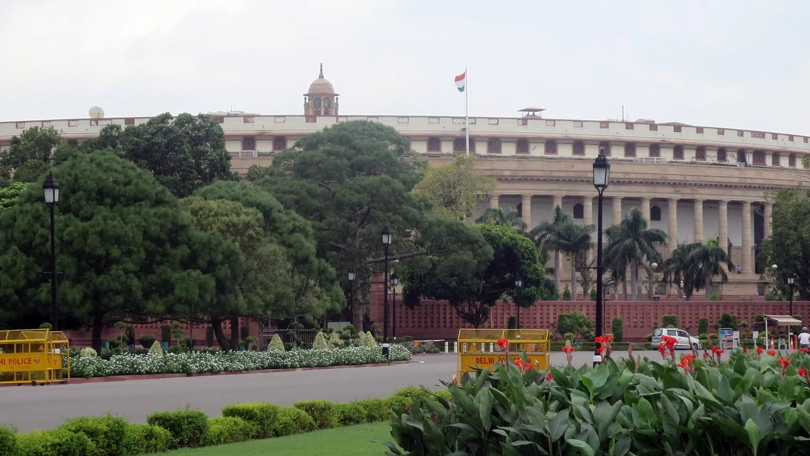 The circular colonnaded Parliament House in New Delhi, the building India's Parliament used until 2023, behind trees and a lawn