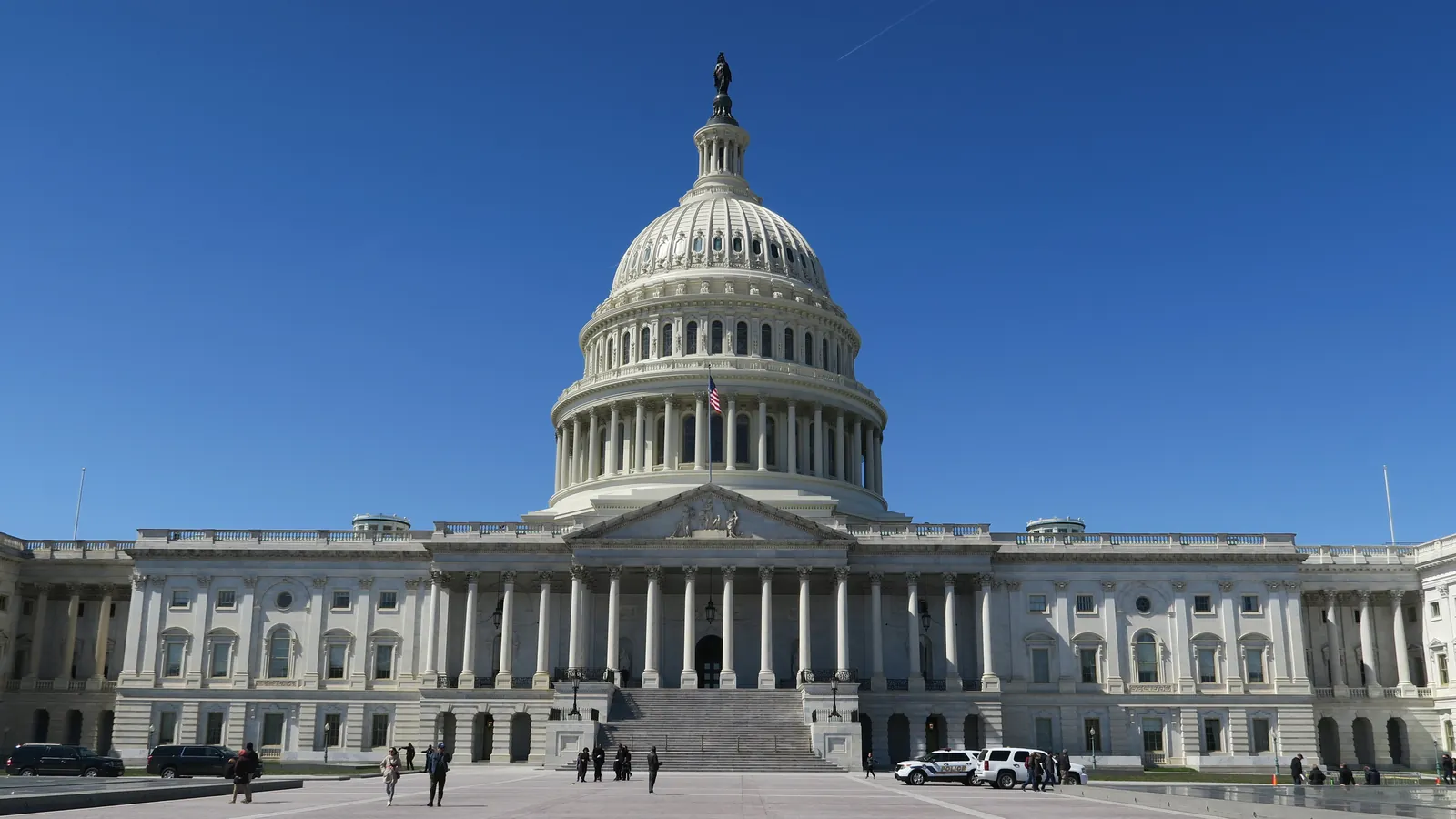 The east front of the United States Capitol in Washington, its white dome above the columned portico, seen across the paved plaza