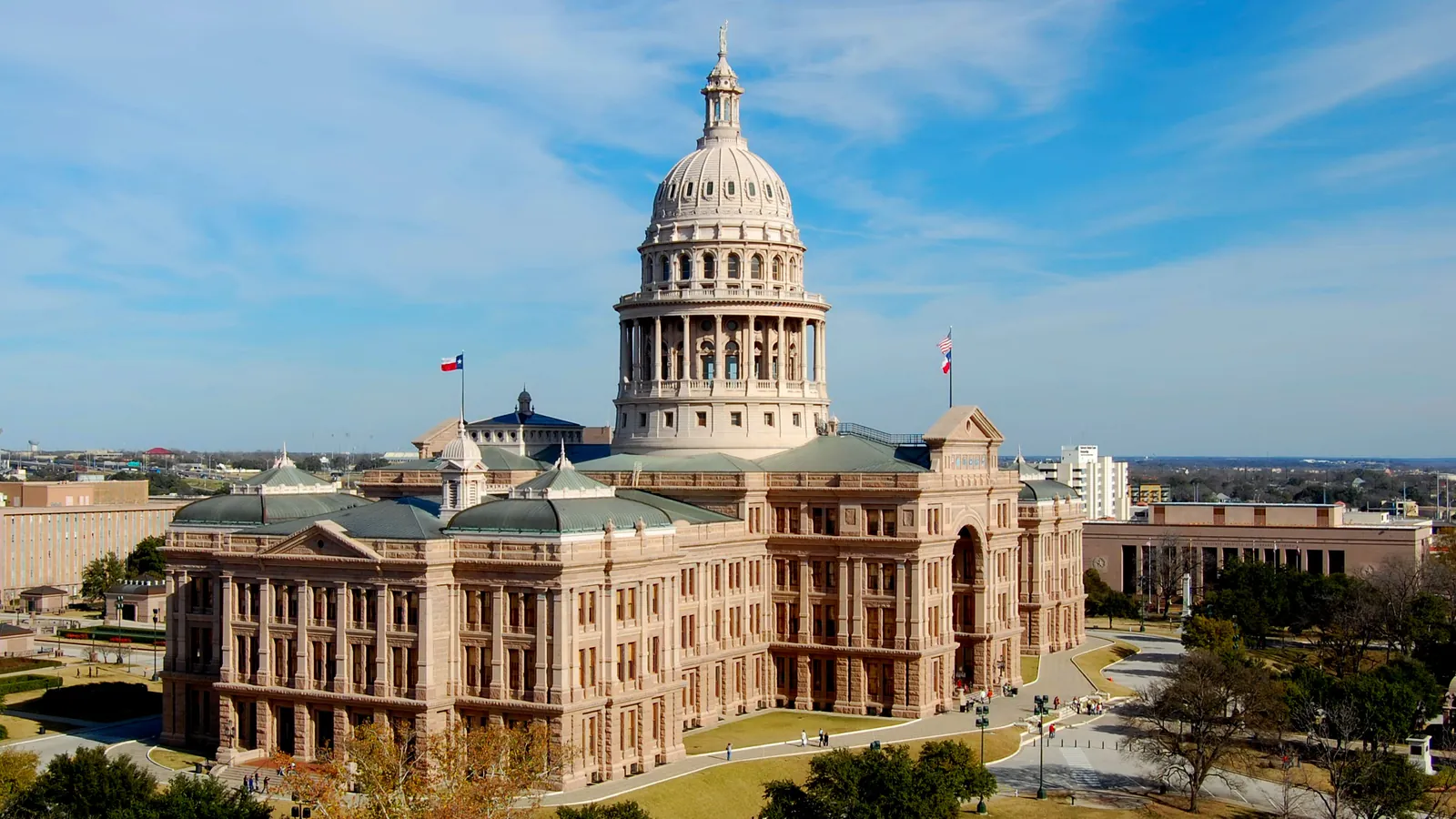 The domed red granite Texas State Capitol in Austin seen from above, with its grounds and the city behind it